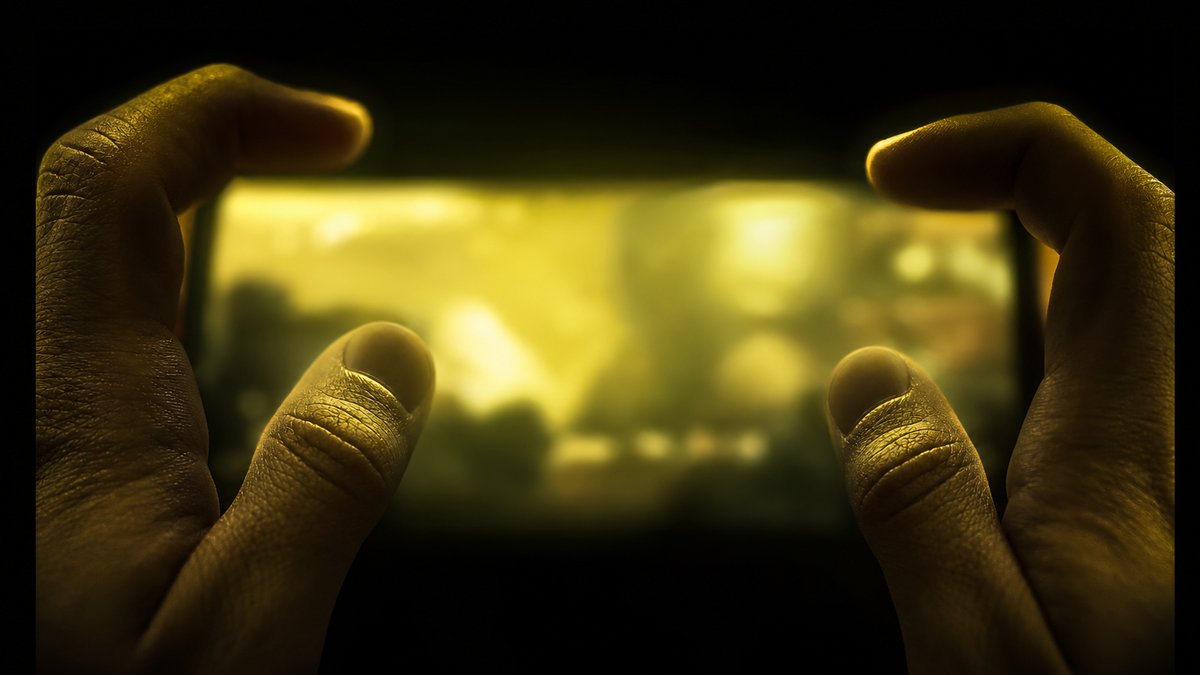 Hands holding a handheld game console, screen glowing softly in the dark.